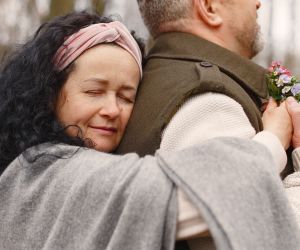 Woman hugging man from behind with flowers.