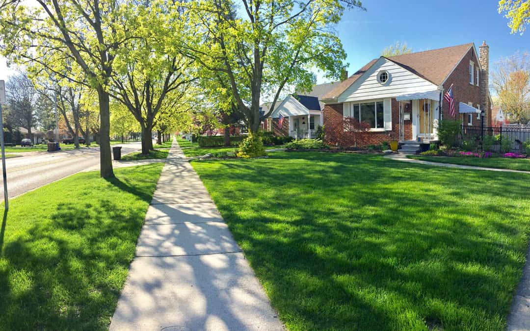 Sidewalk view of a residential neighborhood in summer with brick ranch homes. 