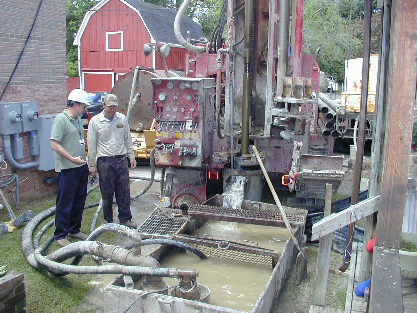 Two people outside working on a water well with machines.