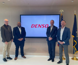 Four men stand in front of TV with DENSO logo.