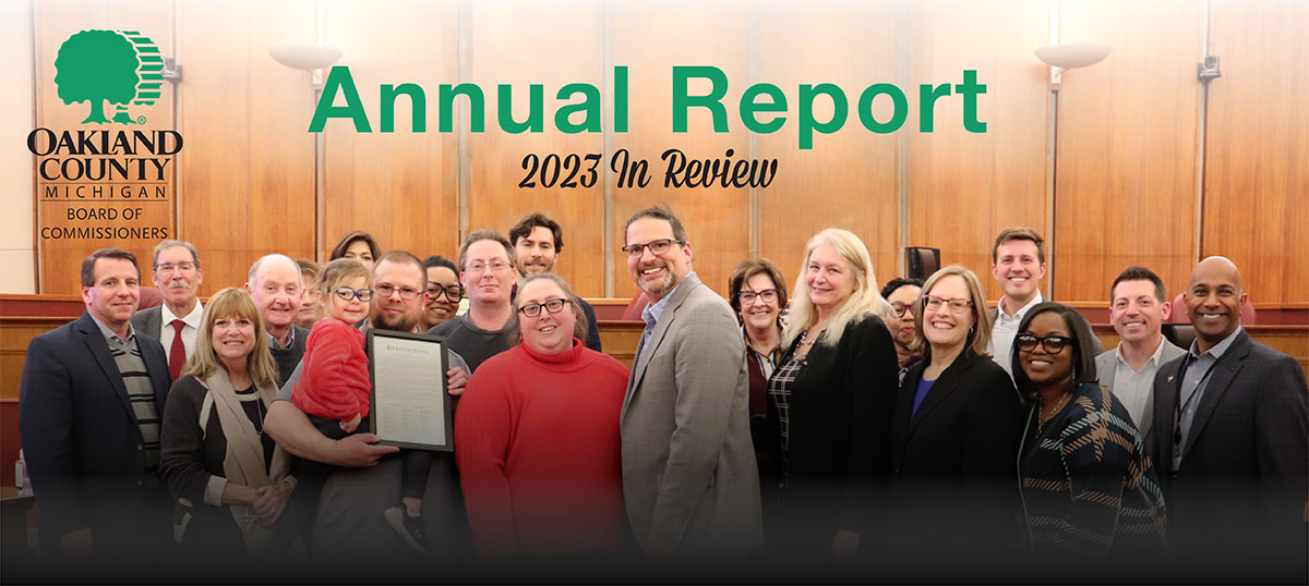 The Oakland County Board of Commissioners, a body of 19 men and women, gather in the auditorium with a family of four to present a proclamation.