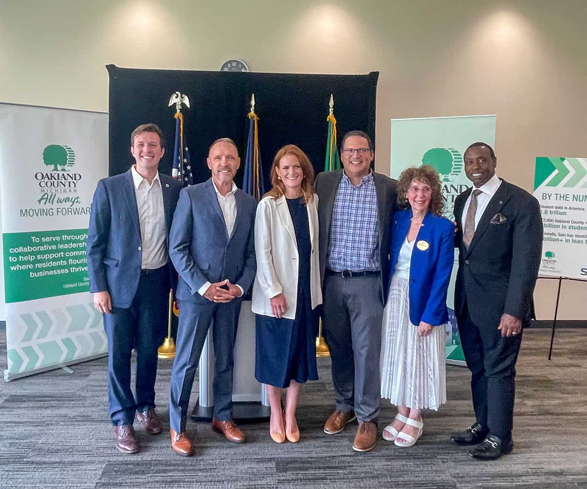 A photo shows a group of Oakland County government and higher education officials at a press conference announcing a student debt relief program with SAVI.