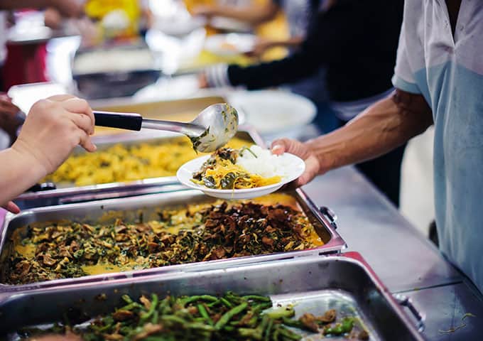 A group of people happily serving food to each other at a buffet, enjoying a variety of delicious dishes together.