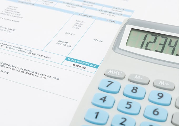 Paper utility bill with a calculator on top of the papers at a desk.