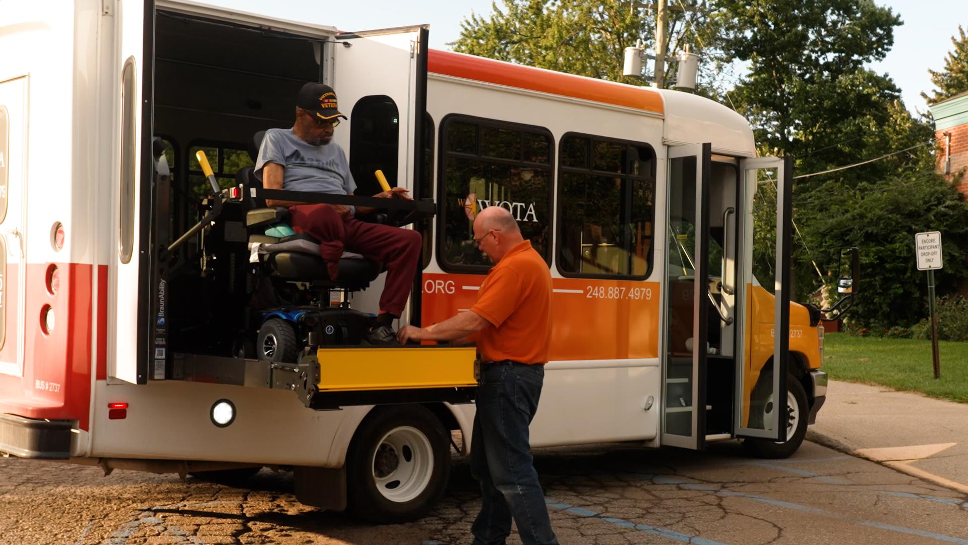 A man dressed in an orange shirt is entering a bus, excited for the ride ahead.