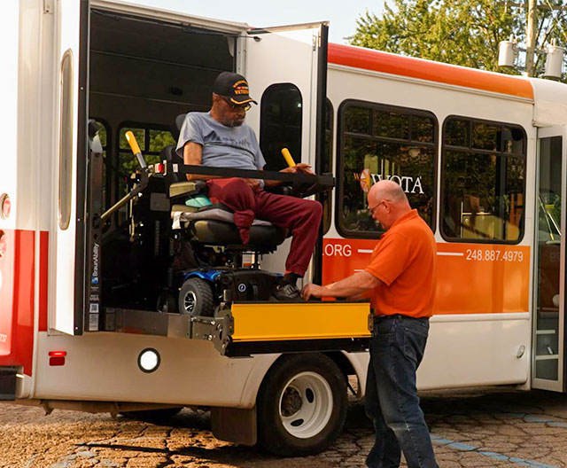 Handicapped male veteran dressed in an orange shirt is getting off a bus, smiling as he leaves.