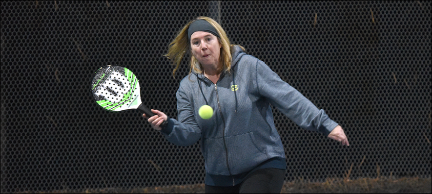 Woman playing platform tennis holding the racquet toward the tennis ball.