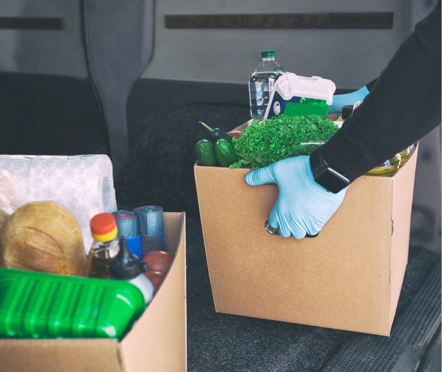 person loading box of food into car trunk