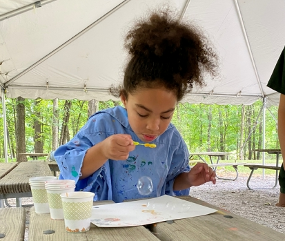 Young girl blowing bubbles to create a craft at an outdoor program.