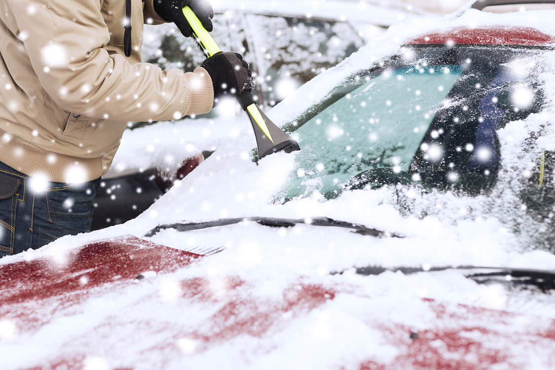 Person scraping snow off car windshield