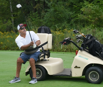 Disabled man swinging golf club from adaptive golf seat on golf cart.